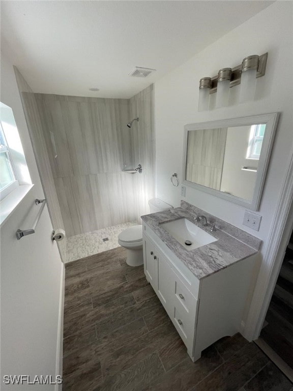 bathroom featuring a tile shower, vanity, wood-type flooring, and toilet