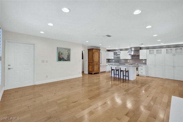 kitchen with a center island, exhaust hood, white cabinets, decorative light fixtures, and a breakfast bar area