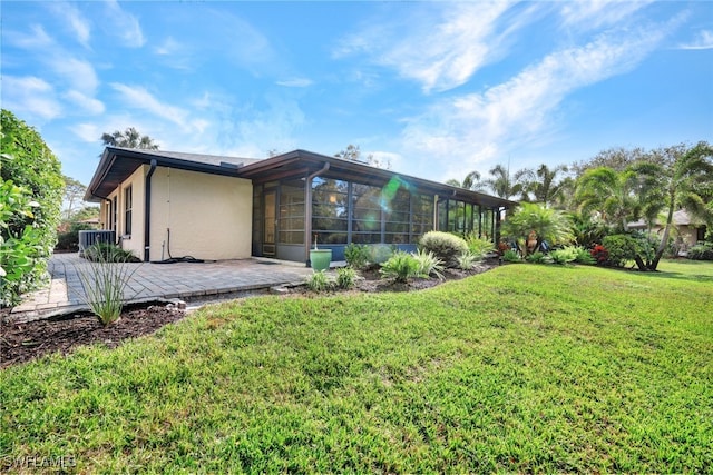 rear view of property featuring a sunroom, central air condition unit, a patio, and a lawn