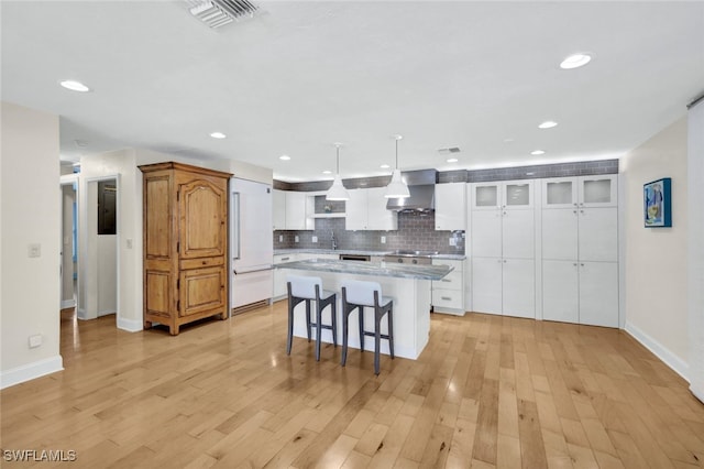 kitchen featuring white cabinets, a center island, wall chimney range hood, and pendant lighting