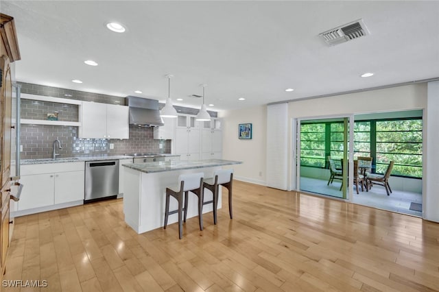 kitchen with pendant lighting, white cabinets, wall chimney range hood, stainless steel dishwasher, and a kitchen island