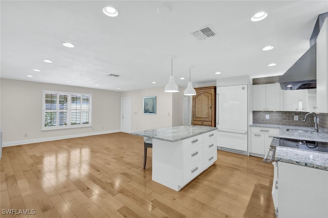 kitchen with a center island, white cabinets, sink, hanging light fixtures, and light wood-type flooring