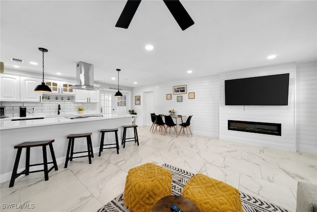 kitchen with pendant lighting, a breakfast bar, a large fireplace, island range hood, and white cabinetry