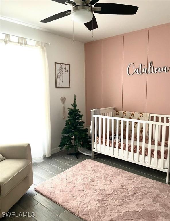 bedroom with ceiling fan, a nursery area, and hardwood / wood-style flooring