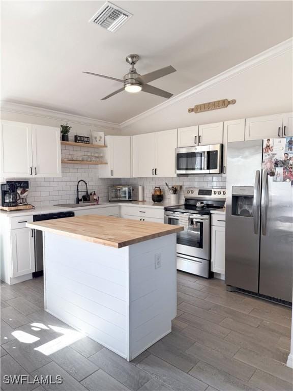 kitchen featuring stainless steel appliances, vaulted ceiling, a center island, white cabinetry, and butcher block counters