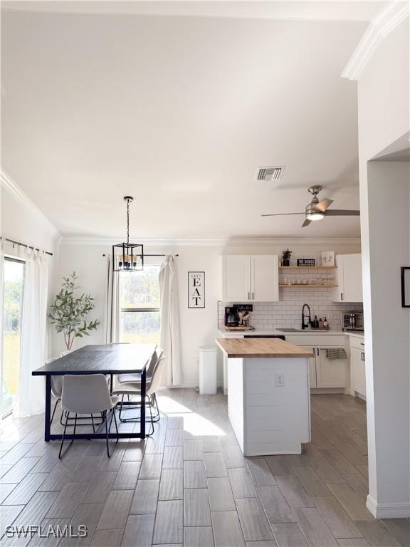 kitchen with a center island, white cabinets, hanging light fixtures, light hardwood / wood-style flooring, and butcher block counters