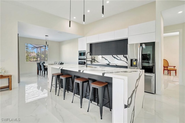 kitchen with decorative light fixtures, white cabinetry, stainless steel appliances, and a large island with sink