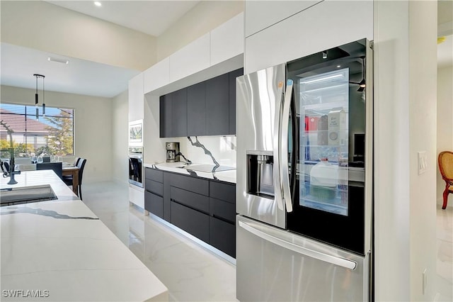 kitchen with appliances with stainless steel finishes, light stone counters, sink, white cabinets, and hanging light fixtures