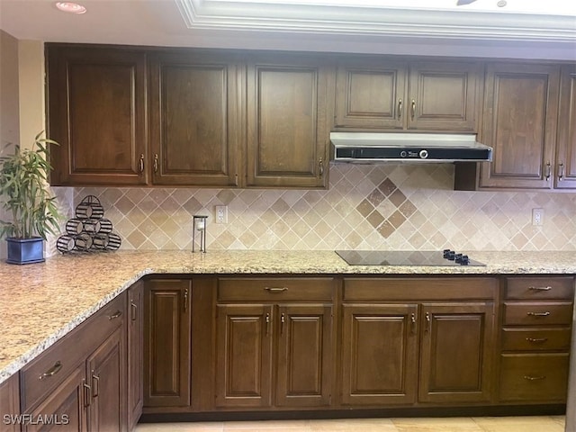 kitchen with black electric cooktop, under cabinet range hood, dark brown cabinets, light stone countertops, and tasteful backsplash