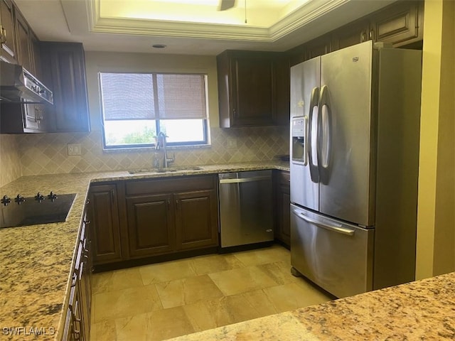 kitchen featuring appliances with stainless steel finishes, a tray ceiling, light stone counters, and sink