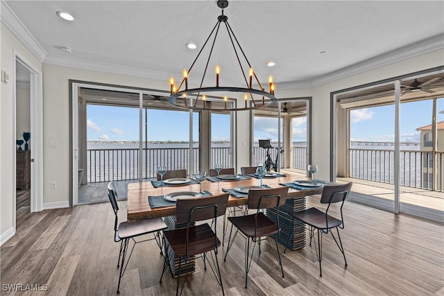 dining area featuring ornamental molding, a textured ceiling, a water view, an inviting chandelier, and hardwood / wood-style floors