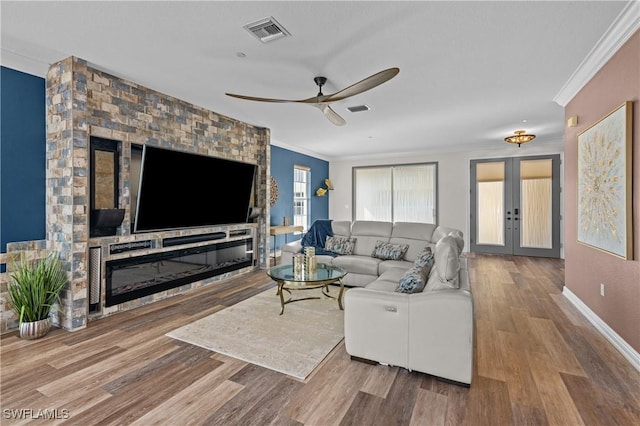 living room featuring hardwood / wood-style floors, french doors, crown molding, ceiling fan, and a fireplace