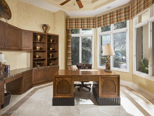 office featuring baseboards, a raised ceiling, a ceiling fan, and a healthy amount of sunlight