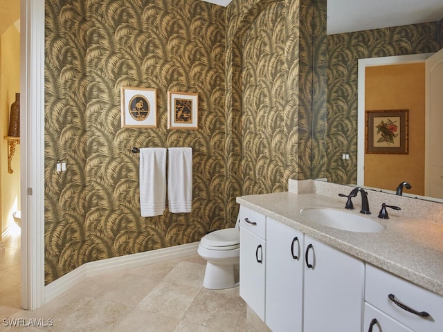 bathroom with toilet, wallpapered walls, baseboards, and vanity