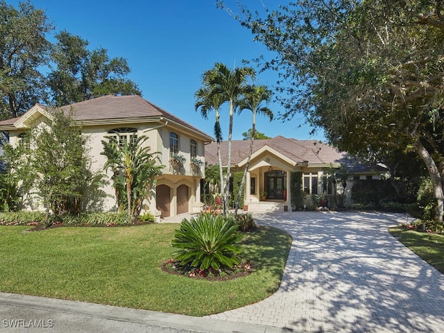 mediterranean / spanish house featuring a tiled roof, decorative driveway, a front yard, and stucco siding