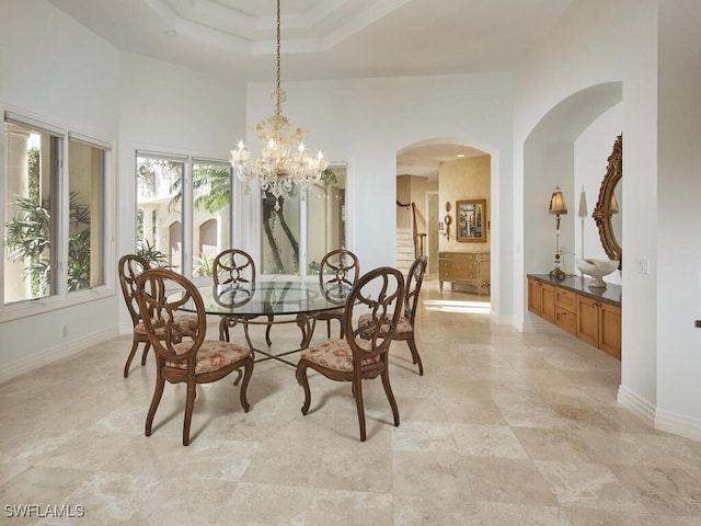 dining space featuring a chandelier, arched walkways, a towering ceiling, baseboards, and a raised ceiling