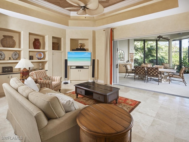 living room featuring ceiling fan, built in features, ornamental molding, a towering ceiling, and a tray ceiling