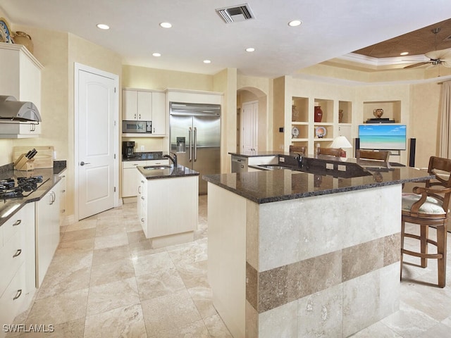 kitchen featuring visible vents, arched walkways, appliances with stainless steel finishes, a large island with sink, and white cabinetry