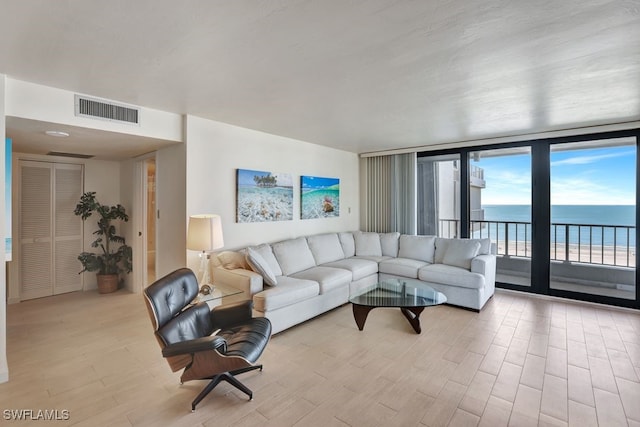 living room featuring light hardwood / wood-style flooring, a water view, and a wall of windows