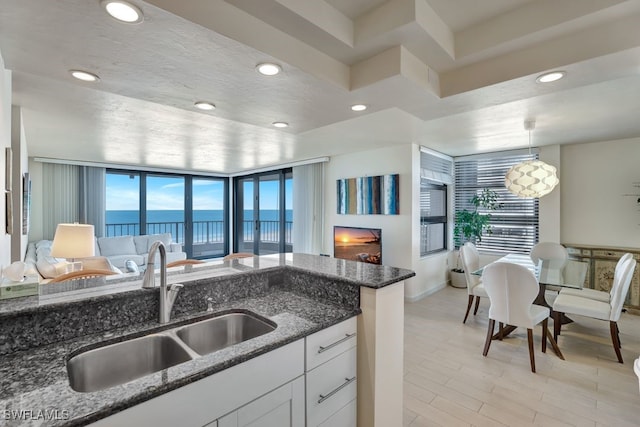 kitchen featuring dark stone counters, white cabinets, sink, hanging light fixtures, and a wealth of natural light