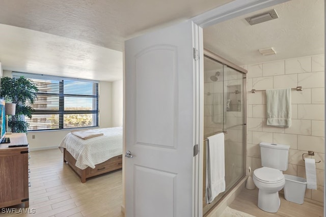 bathroom featuring a textured ceiling, toilet, walk in shower, and tile walls