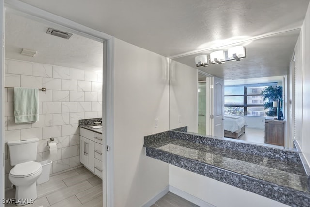 bathroom with vanity, toilet, tile walls, and an inviting chandelier