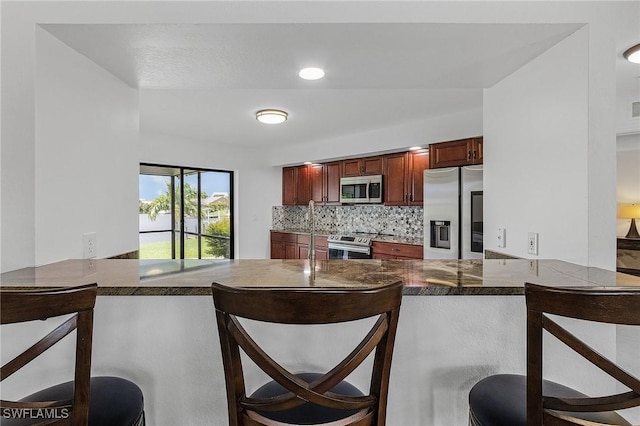 kitchen featuring a kitchen breakfast bar, kitchen peninsula, decorative backsplash, and stainless steel appliances