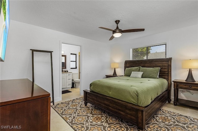 bedroom with ensuite bathroom, ceiling fan, light tile patterned floors, and a textured ceiling