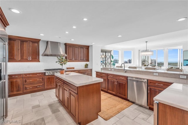 kitchen with a center island, sink, wall chimney exhaust hood, appliances with stainless steel finishes, and decorative light fixtures