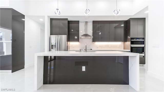 kitchen featuring pendant lighting, wall chimney exhaust hood, stainless steel appliances, and a kitchen island with sink