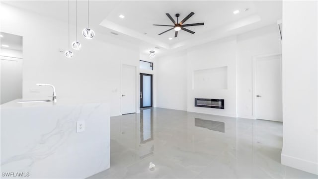 unfurnished living room with a tray ceiling, ceiling fan, and sink