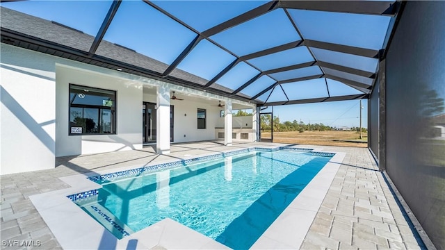 view of pool featuring ceiling fan, a patio, glass enclosure, and an outdoor kitchen