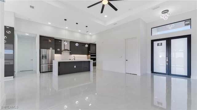 kitchen featuring french doors, ceiling fan, pendant lighting, stainless steel fridge with ice dispenser, and an island with sink