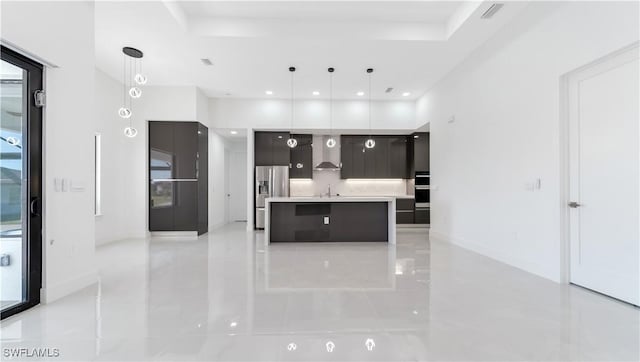 kitchen with stainless steel appliances, sink, wall chimney range hood, pendant lighting, and a center island with sink