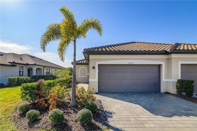 mediterranean / spanish house featuring an attached garage, a tiled roof, decorative driveway, and stucco siding