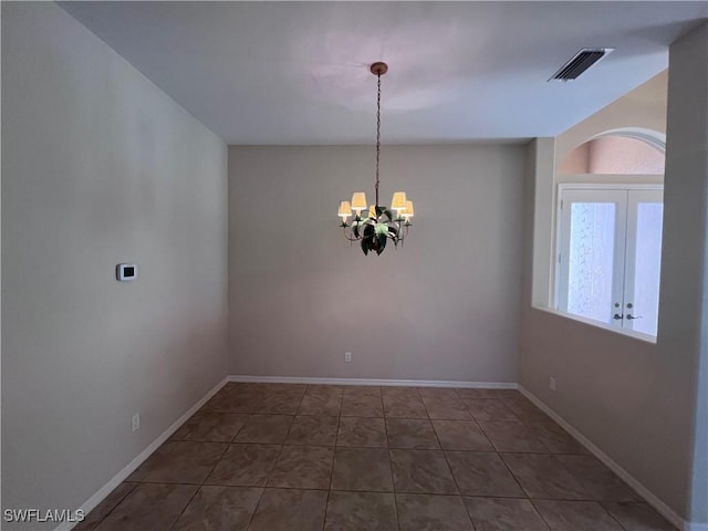 empty room with tile patterned floors, french doors, and a notable chandelier