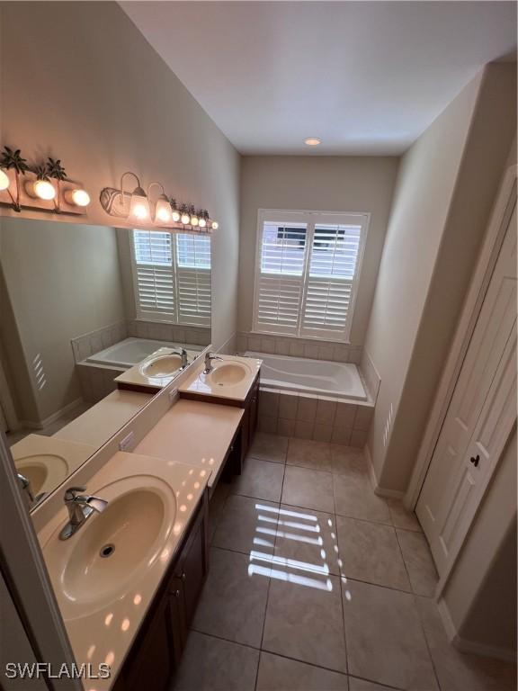 bathroom with tile patterned floors, vanity, and a relaxing tiled tub