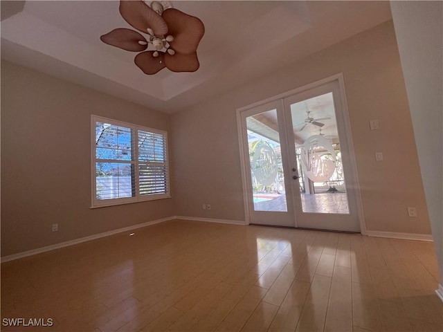 unfurnished room featuring a raised ceiling, ceiling fan, french doors, and light hardwood / wood-style floors