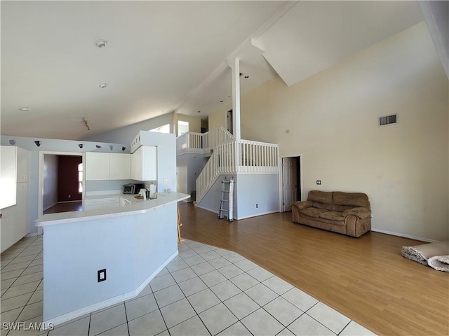 kitchen featuring white cabinets, kitchen peninsula, high vaulted ceiling, and light hardwood / wood-style flooring