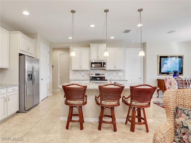 kitchen featuring light stone counters, stainless steel appliances, hanging light fixtures, and an island with sink