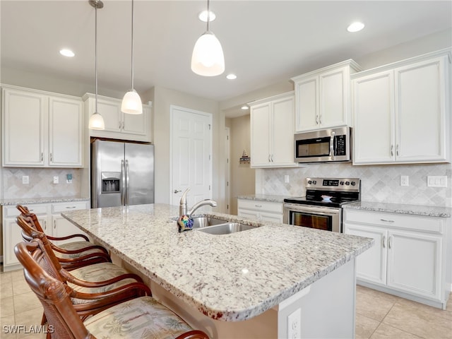 kitchen featuring white cabinetry, sink, stainless steel appliances, decorative light fixtures, and a center island with sink