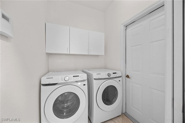 clothes washing area featuring washer and dryer, light tile patterned floors, and cabinets