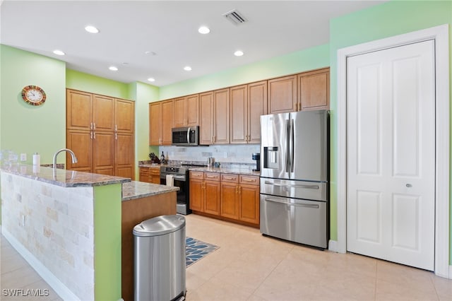 kitchen with sink, stainless steel appliances, kitchen peninsula, dark stone counters, and light tile patterned floors