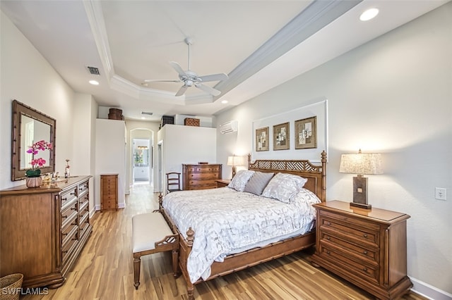 bedroom featuring a wall mounted air conditioner, a raised ceiling, ceiling fan, ornamental molding, and light hardwood / wood-style floors