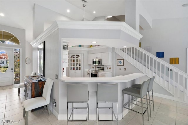 kitchen with high vaulted ceiling, white cabinets, a kitchen breakfast bar, appliances with stainless steel finishes, and light tile patterned flooring