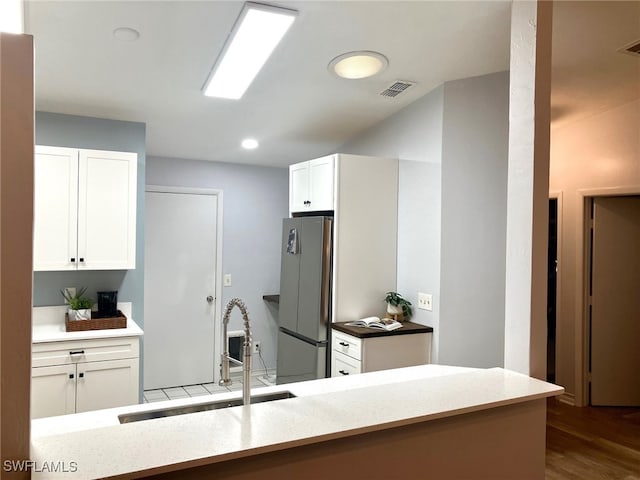 kitchen featuring white cabinetry, sink, kitchen peninsula, and stainless steel refrigerator