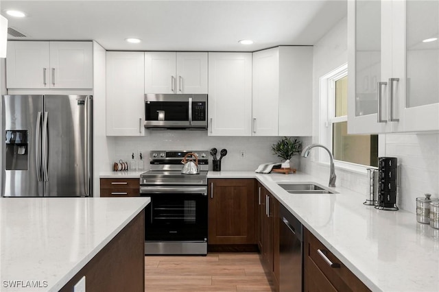 kitchen with tasteful backsplash, stainless steel appliances, sink, light hardwood / wood-style flooring, and white cabinets