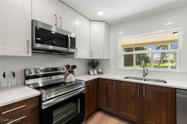 kitchen with sink, light hardwood / wood-style flooring, tasteful backsplash, white cabinetry, and stainless steel appliances