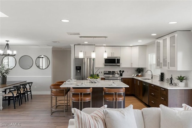 kitchen with light hardwood / wood-style flooring, appliances with stainless steel finishes, decorative light fixtures, a kitchen island, and dark brown cabinets