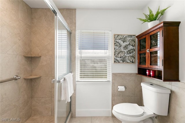 bathroom with tile patterned floors, toilet, a shower with door, and tile walls